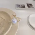 Detalle de elegante pinza de pelo con perlas de acabado irisado en plato de cerámica - Estilo Redondo Champaña