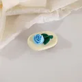 Detailed macro view of a 3D blue tulip hair clip with green leaves on cream base - Blue