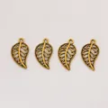 Detailed macro view of four vintage filigree alloy leaf charms for DIY jewelry making - Antique Gold