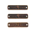 Makroaufnahme von drei bronzefarbenen DIY-Anhängern mit graviertem Handmade-Schriftzug - Handmade Buchstabenschild Stil / Antikes Rotkupfer