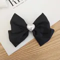 Detail of a black matte bow hair clip with a central white heart pearl on a wooden desk - Fabric Bow With Pearl Heart / Black