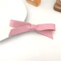 Light pink leather bow hair clip with textured finish placed on a white ceramic plate - Leather Texture / Pink