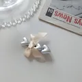 Detail of cream silk bow hair clip with three silver metallic hearts on a newspaper backdrop - Beige