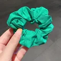 Vibrant green fabric scrunchie with soft pleats shown from a top-down view on gray floor - Green