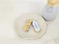 Détail de barrettes en laine jaune avec pompons colorés sur un plateau en céramique - Pinces cheveux bec de canard / Jaune