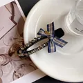 Detailaufnahme einer blauen Karomusterschleife mit Strasssteinen und goldenem Love-Anhänger - Schwarz