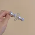 Eleganter goldener Haarclip mit vier weißen Perlen und Perlenbogen in der Hand - Perlen-Seitenclip