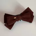 Macro shot of brown suede bow hair clip with gold Love charm and strong black grip - Brown