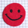 Cute red wool felt round coaster featuring a black stitched smiley face design - Red