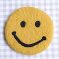Yellow wool felt coaster with a black embroidered smiley face and round soft texture - Yellow