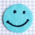 Cute round wool felt coaster in cyan blue with a minimalist black smiley face pattern - Light Blue