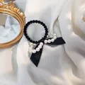 Detailaufnahme von schwarzem Haargummi mit Schleife und weißen Perlen auf Chiffon-Stoff - Schwarze Schleife Haargummi