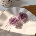 Gros plan de deux pinces à cheveux fleurs en maille violette avec perles dans un plat blanc - Camélia Violet
