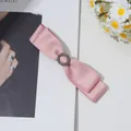 Détail de la barrette à double nœud en satin rose avec strass vintage sur fond de magazine - Rose