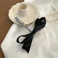 Elegante pasador de lazo negro con diamantes de imitación sobre fondo de seda blanca - Estilo de Circonita Multicolor / Multicolor