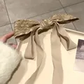 Detailed texture of a vintage bow hair clip with golden brocade and long cream ribbons - Khaki
