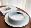 Nahaufnahme eines hellblauen Plüsch-Haarreifs mit Hand Made Etikett auf Keramikteller - Blau