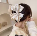 Detail of a large cream satin bow hair claw clip worn on hair for a French vintage look - White