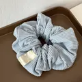 Detail view of a light blue corduroy hair scrunchie with FMdred woven label in a tray - Blue