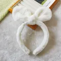 Detail shot of white plush bow headband on wooden tray with soft textures - White Rabbit Ears