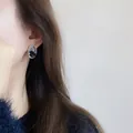 Minimalistische zilveren oorknopjes met zwart-witte steeninleg op een vrouwelijk model - Zwarte glinsterende diamant oorknopjes