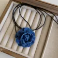 Dettaglio della collana girocollo con camelia in denim su espositore in legno per gioielli - Denim Blu Scuro Piccolo