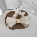 Detailed view of an elegant organza bow hair scrunchie in creamy white on a leather surface - Cream