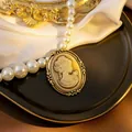 Detailed macro of vintage relief pendant on white pearl necklace over satin background - Yellow