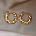 Gros plan de boucles d'oreilles créoles dorées texture lave sur tissu en soie champagne - Or