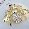 Elegant gold bee brooch with white rhinestones on a decorative white shell background - Gold