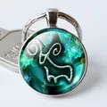 Detalle de llavero metálico redondo con fondo floral verde azulado y signo Capricornio - Tótem de Cabra Cian (Estilo 8)