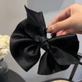 Large black satin bow hair claw clip with elegant silk gloss shown held in hand - Black