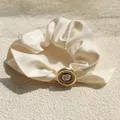 Detail of elegant cream silk scrunchie with rose button and sparkling rhinestone accents - Off White