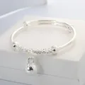 Detail shot of silver baby bangle with hollow flower beads and bell charm on white box - Silver