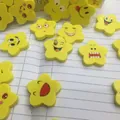 Gelbe sternförmige Radiergummis mit verschiedenen Comic-Smiley-Ausdrücken auf Notizpapier - Stern Emoji Stil / Gelb