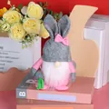 Rosa und grauer Osterhase-Gnom mit Schlappohren, der eine grüne Karotte als Deko hält - Graue Mütze Gesichtslos Puppe