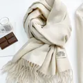 Primo piano di una sciarpa beige tipo cashmere con trama fine e bordi a frange - Bianco Riso