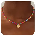 Détail d'un collier de perles colorées avec un pendentif rond doré gravé de la lettre U - Lettre U