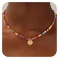 Détail d'un collier de perles multicolores avec un pendentif doré gravé de la lettre X - Lettre X