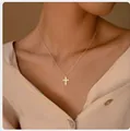 Gros plan détaillé d'un collier croix doré avec pierres incrustées porté par un mannequin - Style Croix Incrustation Carrée Doré (x560) / 14k / Or