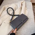 Sac bandoulière gris foncé avec sangle tressée et boucle carrée sur fond de laine - Gris