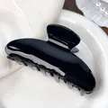 Glossy black acetate hair claw clip with large half-moon design on a white ceramic plate - Solid Black / 9cm