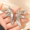 Silberne Ohrringe in Blattform mit Hammerschlag-Textur auf glänzendem Satin-Hintergrund - Silber