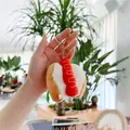Close-up of a plush hot dog keychain with metal ring held by a hand over plants - Hotdog (Standard Chain) / 8cm - 10cm