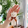 Detailed close-up of cream plush teddy bear charm with a Love ribbon and silver chain - 10.5cm / Coffee Bow / Off White
