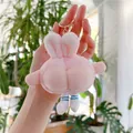 Detail of pink plush rabbit keychain with funny peach butt design held against plants - Pink With Gold Clasp