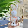 Close-up of mini plush bunny in floral dress held in hand as a backpack accessory - Hanging Chain / Yellow