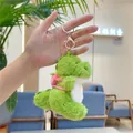 Close-up of green plush dinosaur keychain with pink backpack and metal clasp - Strawberry Backpack Dinosaur / Gold Clasp