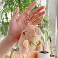 Capybara plush keychain with green bow tie held in hand in a bright garden setting - Green Bowtie Style (Gold Clasp)