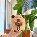Dettaglio di un peluche capybara con fiocco marrone e perline nere tenuto in mano - Catena Pendente / Marrone Scuro